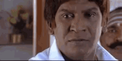 a man with a mustache and a white shirt is making a funny face in a room .