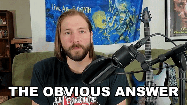 a man with a beard stands in front of a microphone with the words " the obvious answer " above him