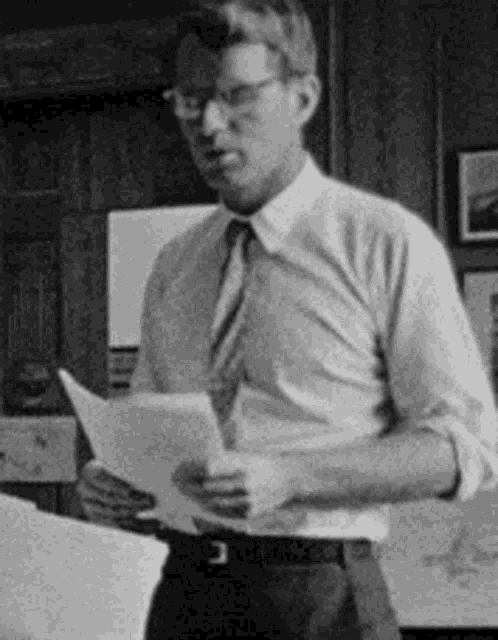 a man in a white shirt and tie is holding a piece of paper in his hands .