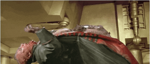 a man is laying on his back in a room with a red cape on .