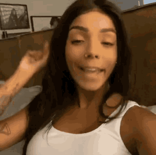 a woman wearing a white tank top and a nose ring is making a funny face