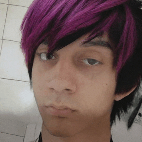 a young man with purple and black hair is looking at the camera