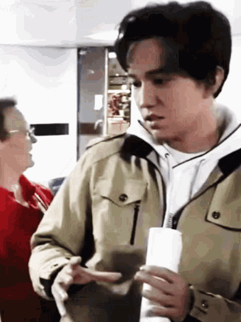 a man in a khaki jacket is holding a white paper in his hand