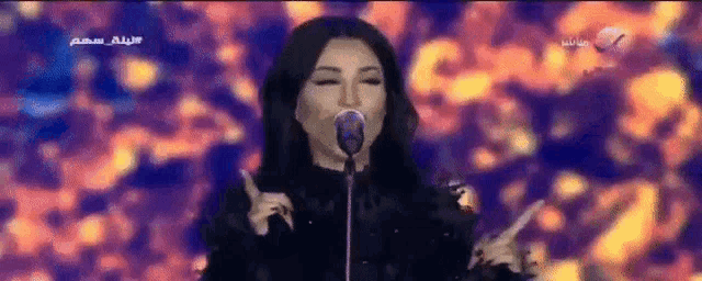a woman singing into a microphone with arabic writing on the screen