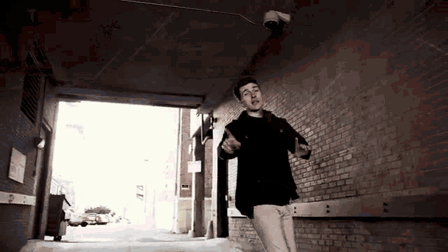 a man in a black jacket and white pants is dancing in an alley