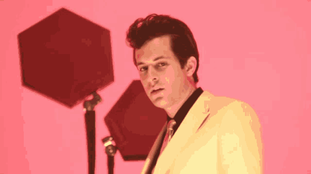 a man in a yellow suit stands in front of a pink background