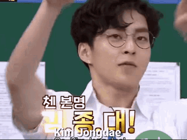 a young man wearing glasses and a white shirt is standing in front of a green board with chinese writing on it .