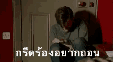 a man is crying while sitting on a couch in front of a door in a room in a foreign language .