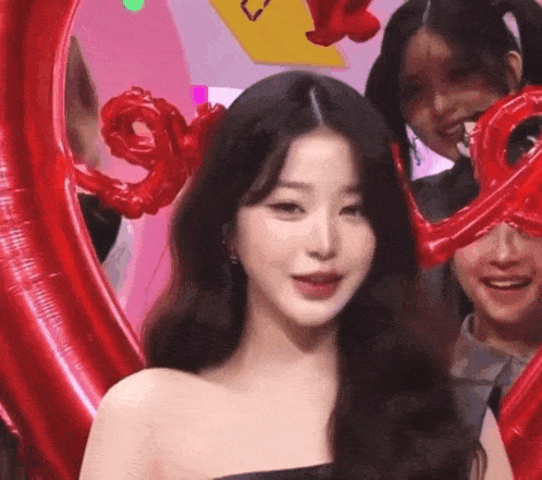 a woman is standing in front of a group of red balloons and smiling .