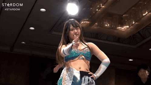 a woman in a wrestling outfit is pointing at the camera with the word stardom behind her