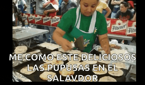 a woman in a green apron is cooking tortillas on a tray in front of a crowd .