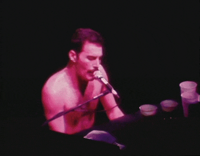 a man without a shirt is singing into a microphone while playing a piano .