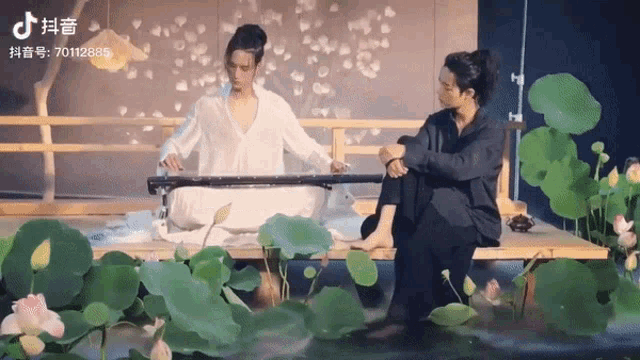 a man is playing a musical instrument while another man sits on a bench surrounded by lotus flowers