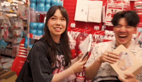 a man and a woman are laughing in front of a wall of party supplies