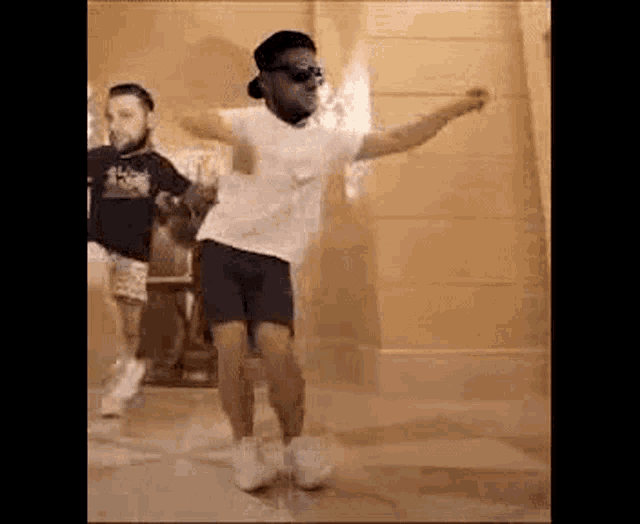 a man in a white shirt and shorts is dancing with another man in a black shirt .