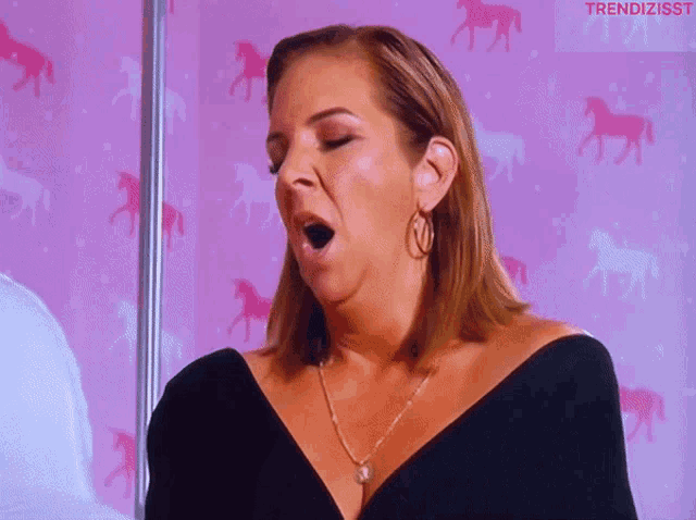 a woman is yawning in front of a pink background with horses