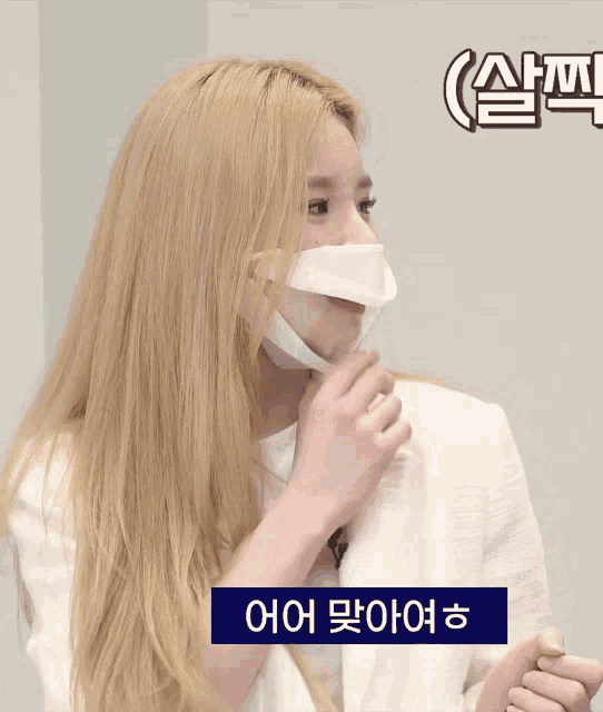 a blonde woman wearing a face mask with korean writing behind her