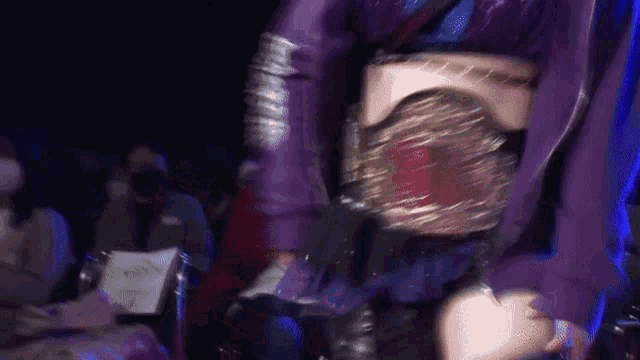 a woman in a purple dress is holding a wrestling belt .