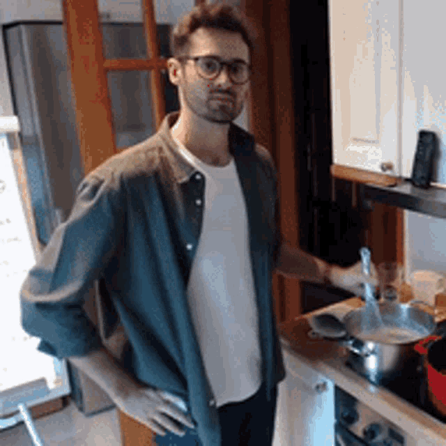 a man wearing glasses and a green shirt is standing in a kitchen