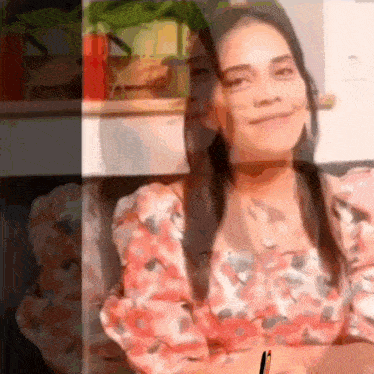 a woman in a pink floral shirt is smiling and holding a pen .