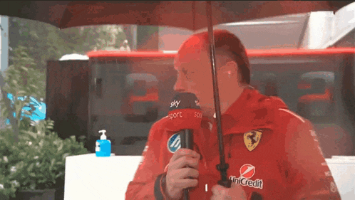 a man in a red jacket is holding an umbrella and a microphone with the word sky on it