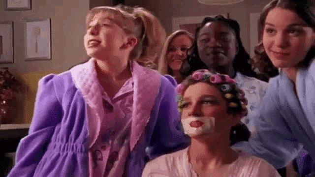 a group of girls are standing around a girl with curlers in her hair and a bandage on her mouth .