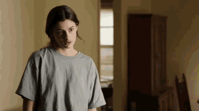 a woman in a grey shirt is standing in a dark room