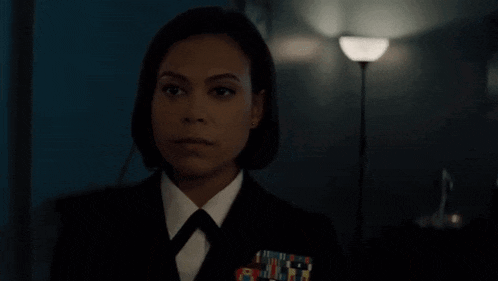 a woman in a military uniform and tie is standing in a dark room .