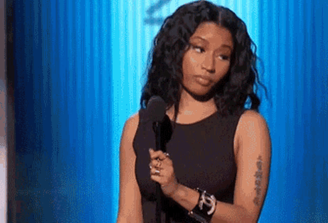 a woman in a black dress is holding a microphone and making a face .