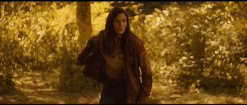 a woman in a brown jacket is standing in the woods