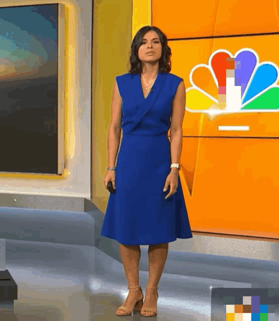 a woman in a blue dress and heels stands in front of a nbc logo