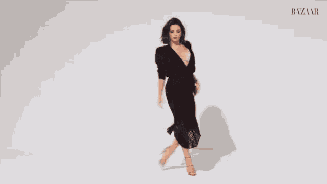 a woman in a black dress and pink heels is dancing in front of a white background .