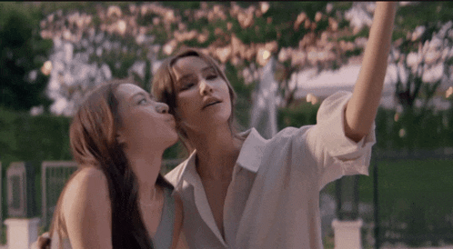a woman kisses another woman on the cheek while they take a selfie
