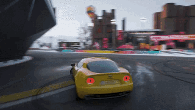 a yellow car is driving down a wet road with a building in the background