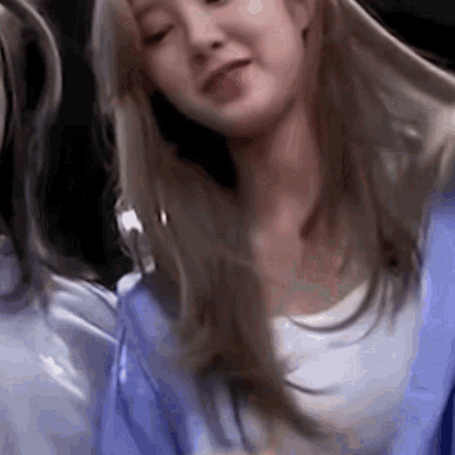 a close up of a woman with long blonde hair wearing a blue shirt and earrings .