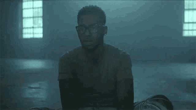 a man wearing glasses is laying on the floor in a dark room