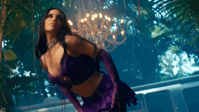 a woman in a purple dress and gloves is standing in front of a chandelier .