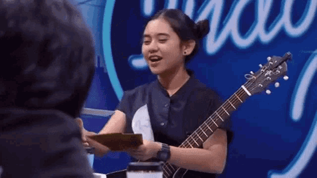 a girl is holding a guitar in front of a sign that says makasih .