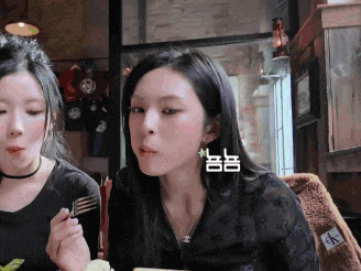 two women are sitting at a table with a fork in their hand and one has a calvin klein jacket on