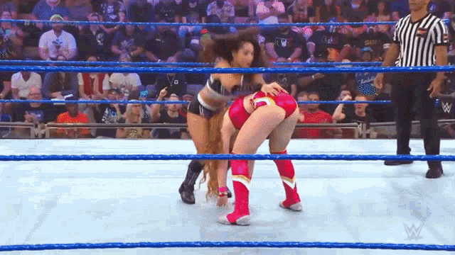two women are wrestling in a wrestling ring with a referee watching