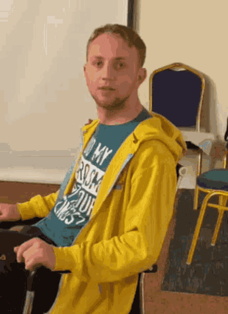 a man in a yellow jacket is sitting in a chair with a purple chair in the background .