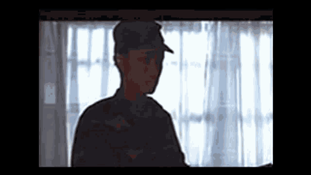 a man in a military uniform is standing in front of a window with curtains .