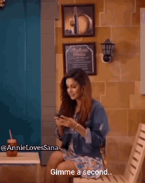 a woman sitting in a chair looking at her phone with the words gimme a second