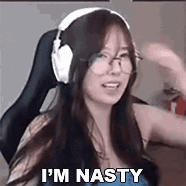 a woman wearing headphones and glasses is saying `` i 'm nasty '' while sitting in a chair .