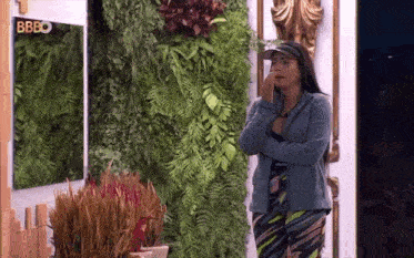 a woman standing in front of a wall with plants and a sign that says bbeo on it