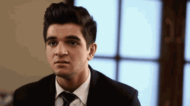 a young man wearing a suit and tie looks at the camera