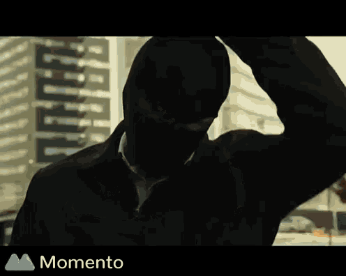 a silhouette of a man wearing a black jacket and a mask with the word momento below him