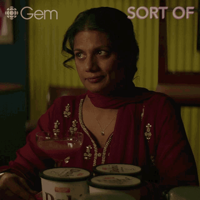 a woman is sitting at a table holding a glass of juice in front of a sign that says " gem "
