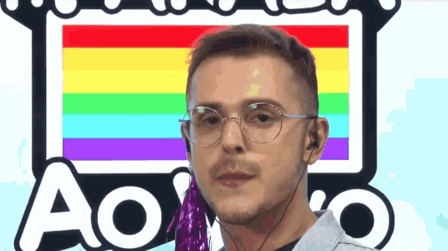 a man wearing glasses and headphones stands in front of a rainbow flag and the word ao