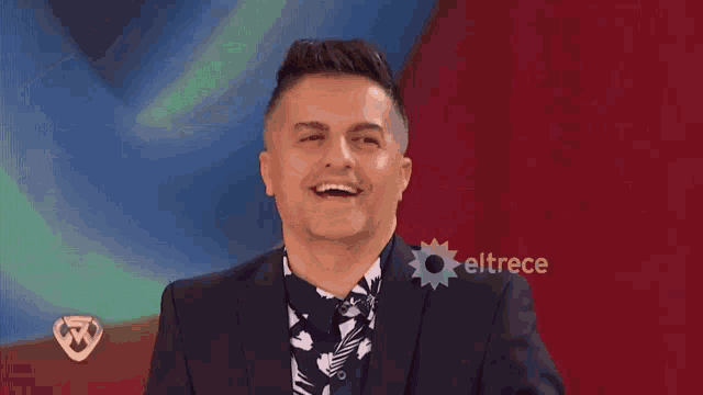 a man in a suit is smiling in front of a sign that says eltrece on it